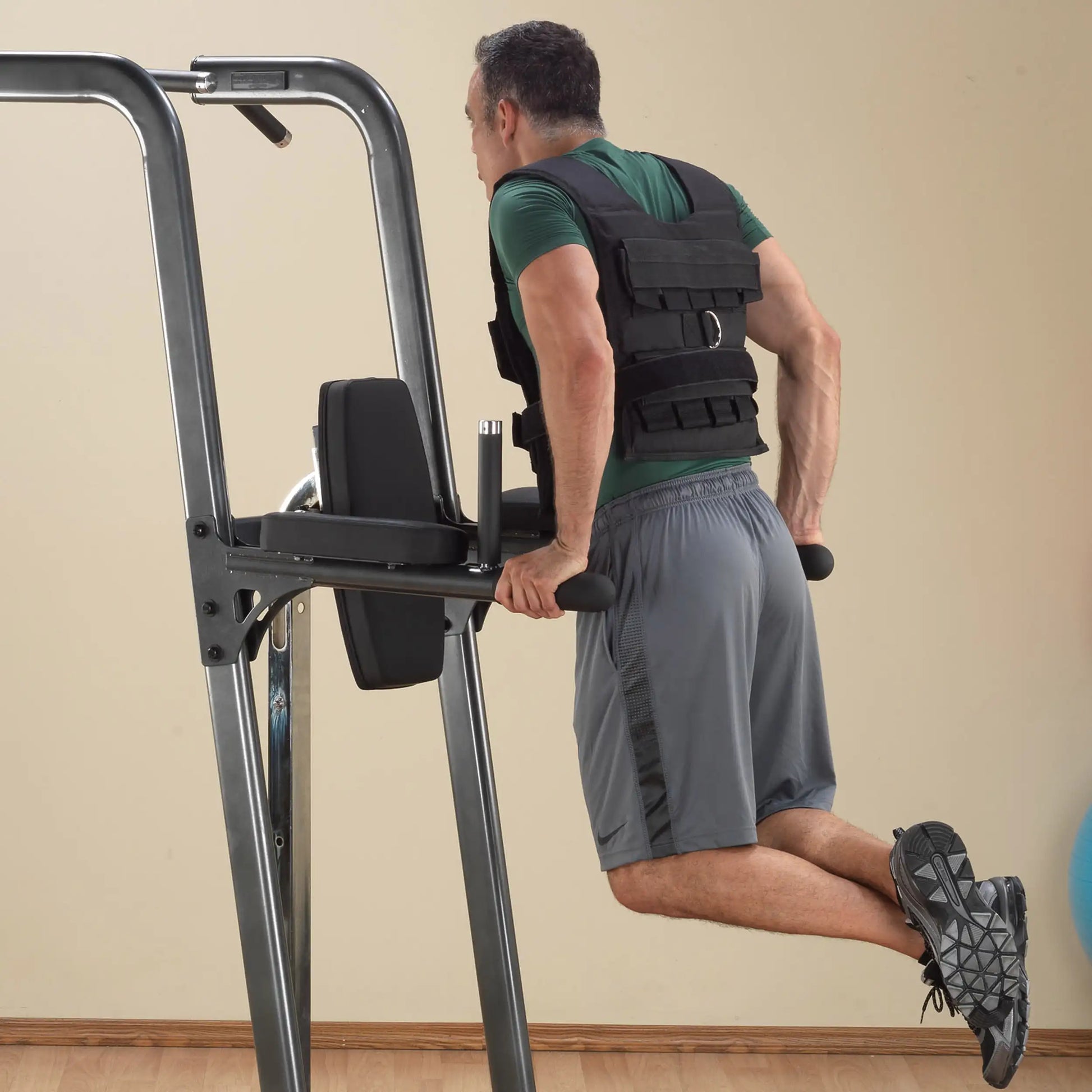 Man using dip station wearing black weighted vest for strength training.