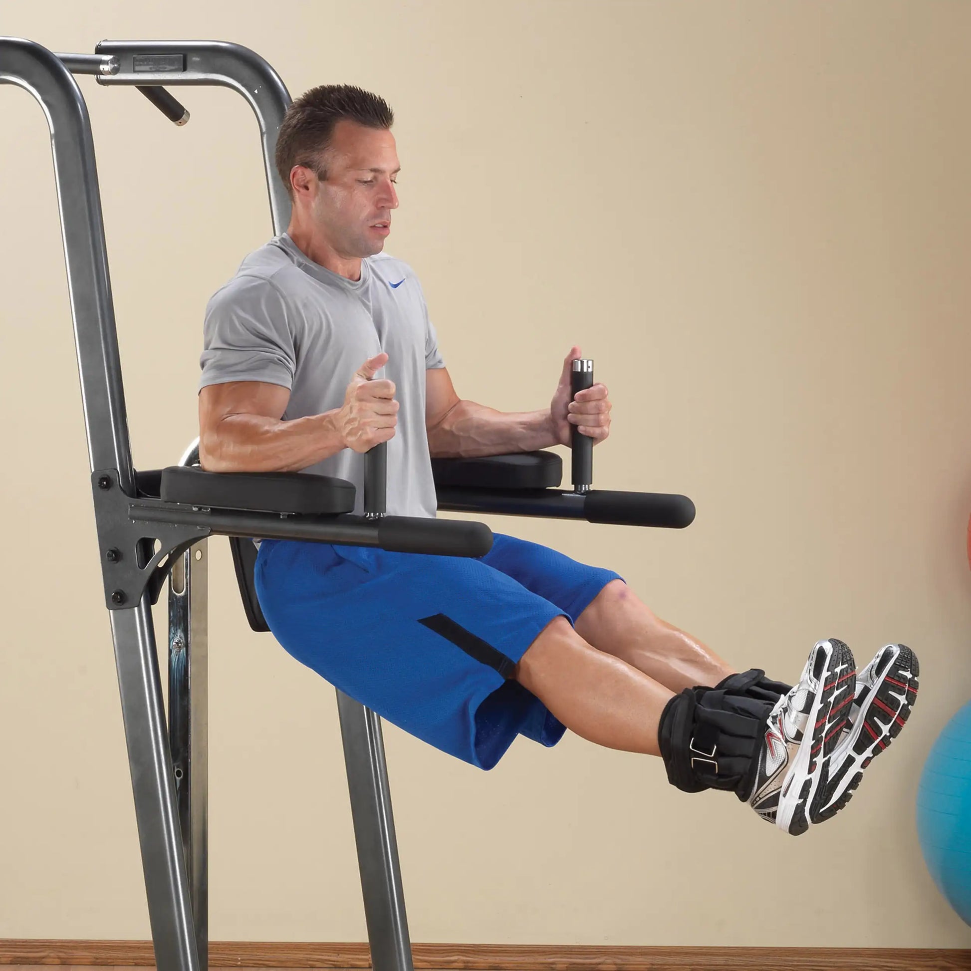 Man doing leg raises on a power tower, wearing blue shorts and ankle weights, showcasing home gym workout.