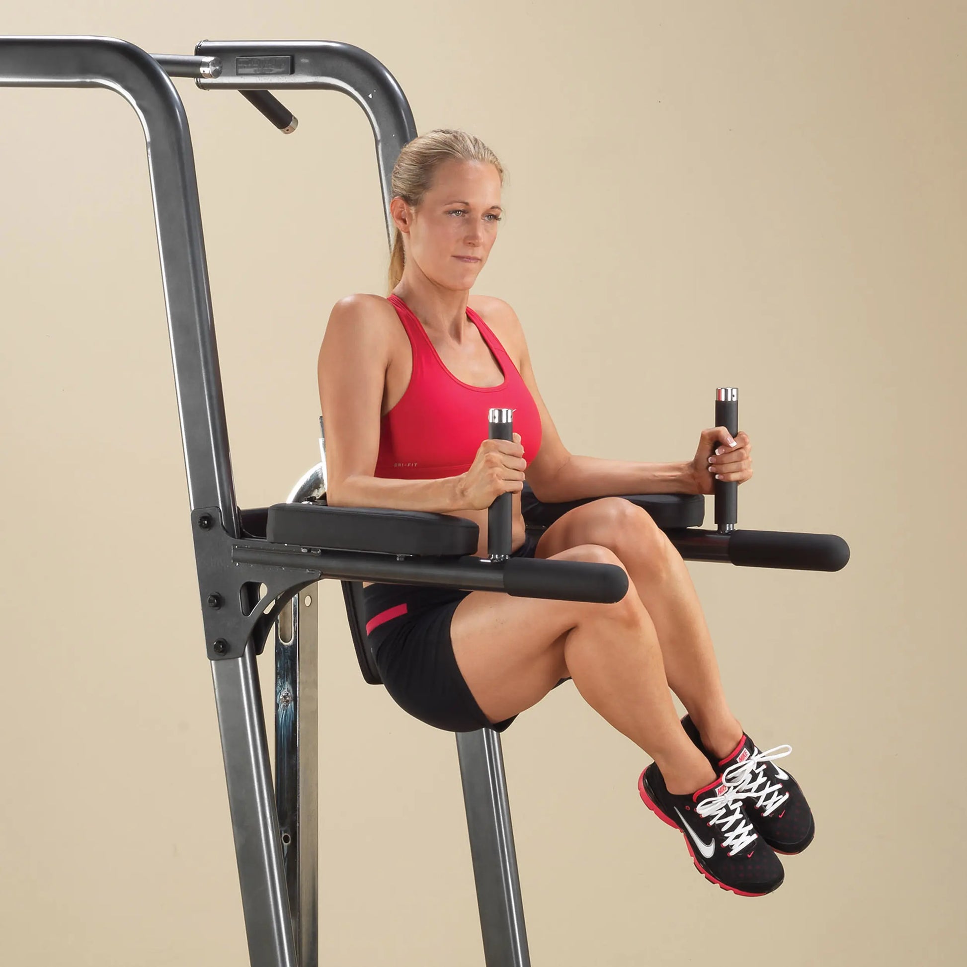 Woman using power tower for knee raises in red tank top.