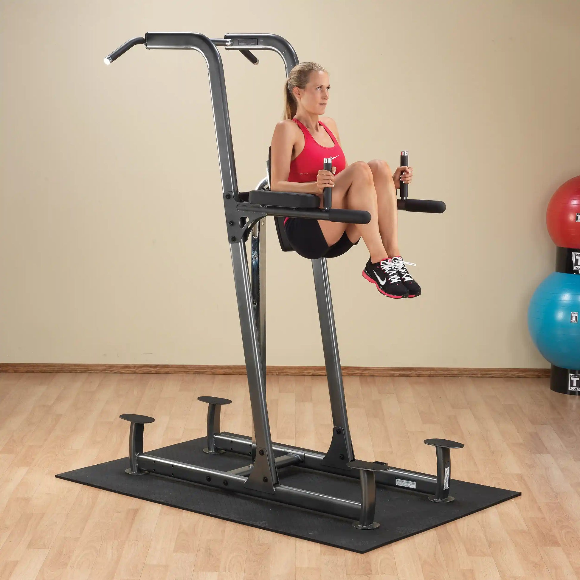Woman using power tower for knee raises in a home gym.