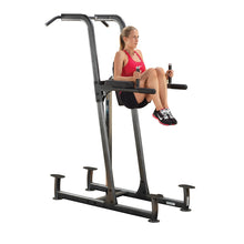 Woman using a Power Tower for knee raises, wearing a red tank top and black shorts.