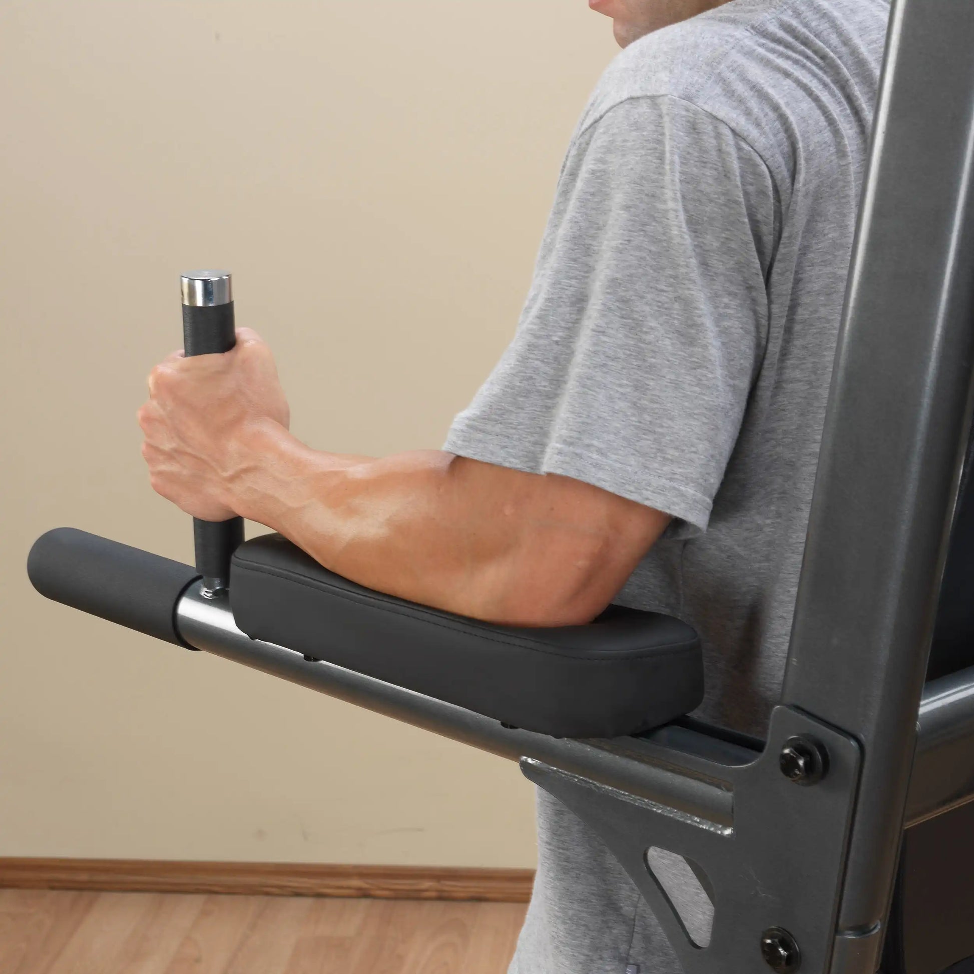 Man using a padded arm workout station, wearing a gray shirt, focusing on tricep exercises.