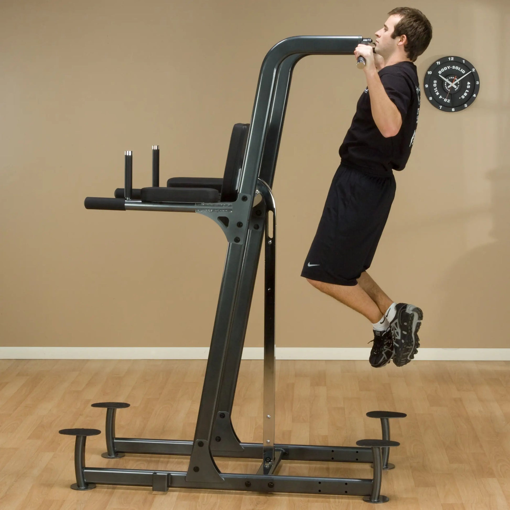 Man using a Body-Solid power tower for pull-ups in a home gym.