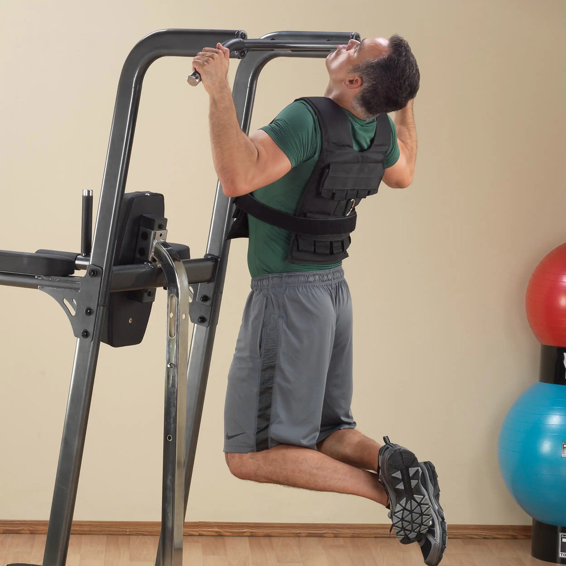 Man doing pull-ups wearing a black weighted vest on a home gym power tower.