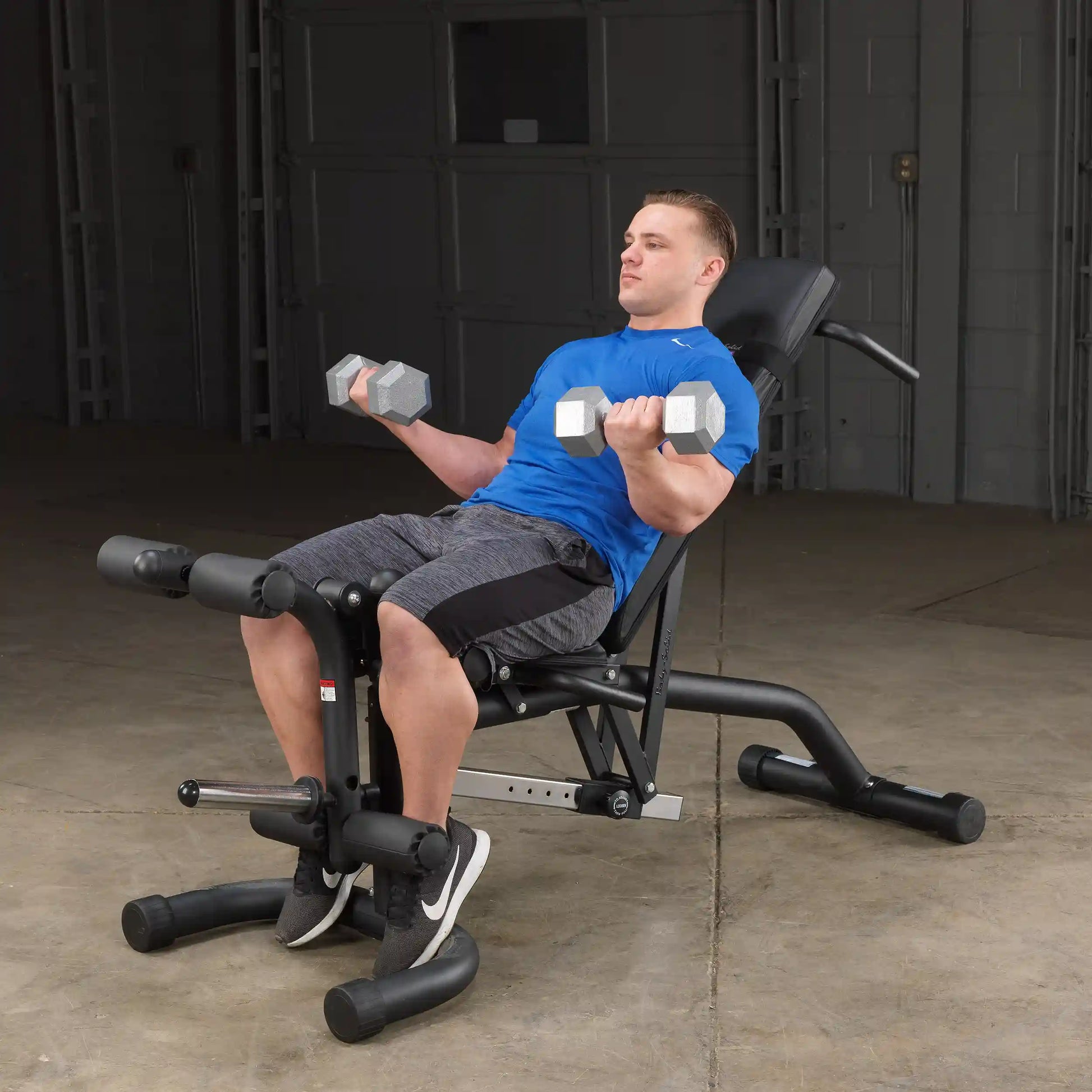 Man in blue shirt lifting dumbbells on adjustable weight bench in gym.