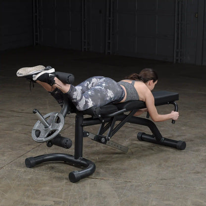 Woman using adjustable weight bench for leg curls in gym.