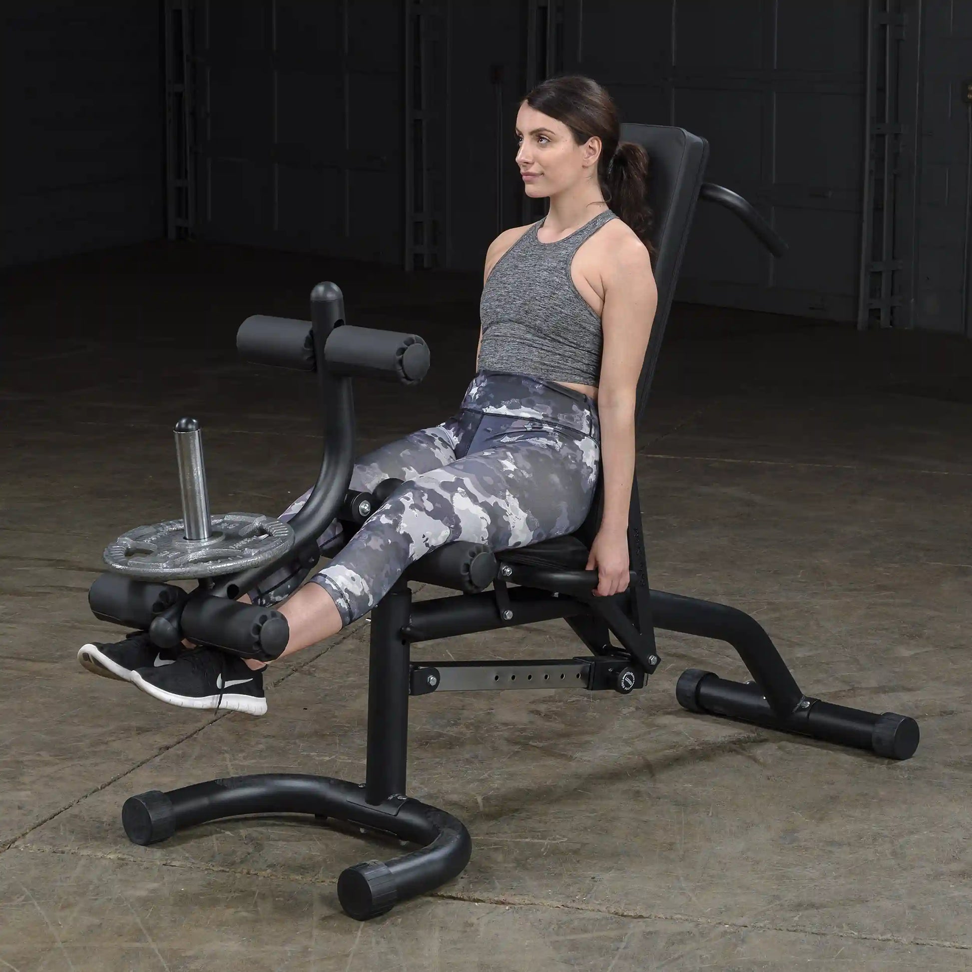 Woman using leg extension machine in gym, wearing gray camo leggings.