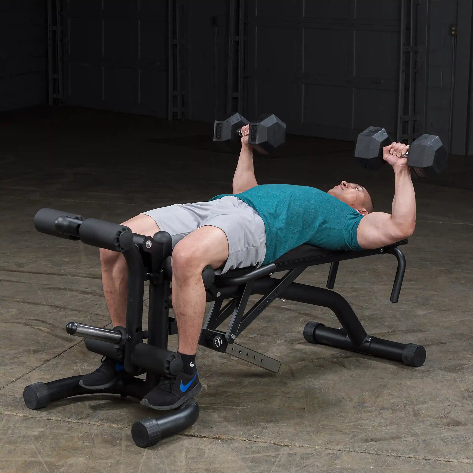Man performing dumbbell bench press on adjustable weight bench in a teal shirt and gray shorts.