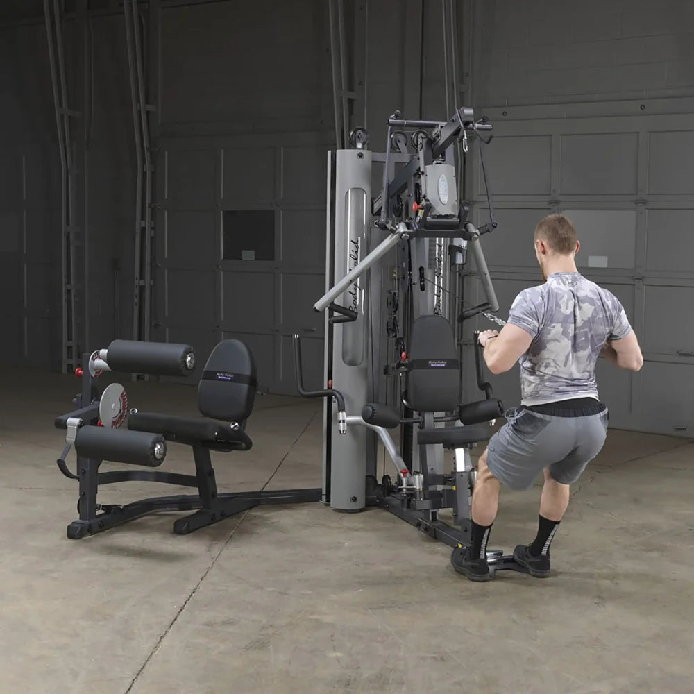 Man using a Body-Solid gym machine for strength training in a spacious garage.