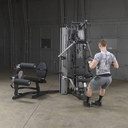 Man using a Body-Solid gym machine for strength training in a spacious garage.