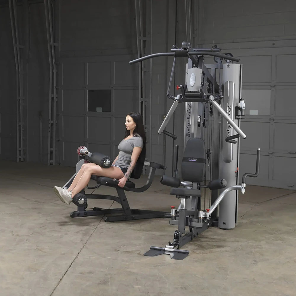 Woman using Body-Solid gym equipment for leg exercises in a garage setting.
