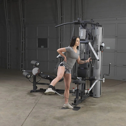 Woman exercising on Body-Solid home gym, performing leg curl with ankle strap.