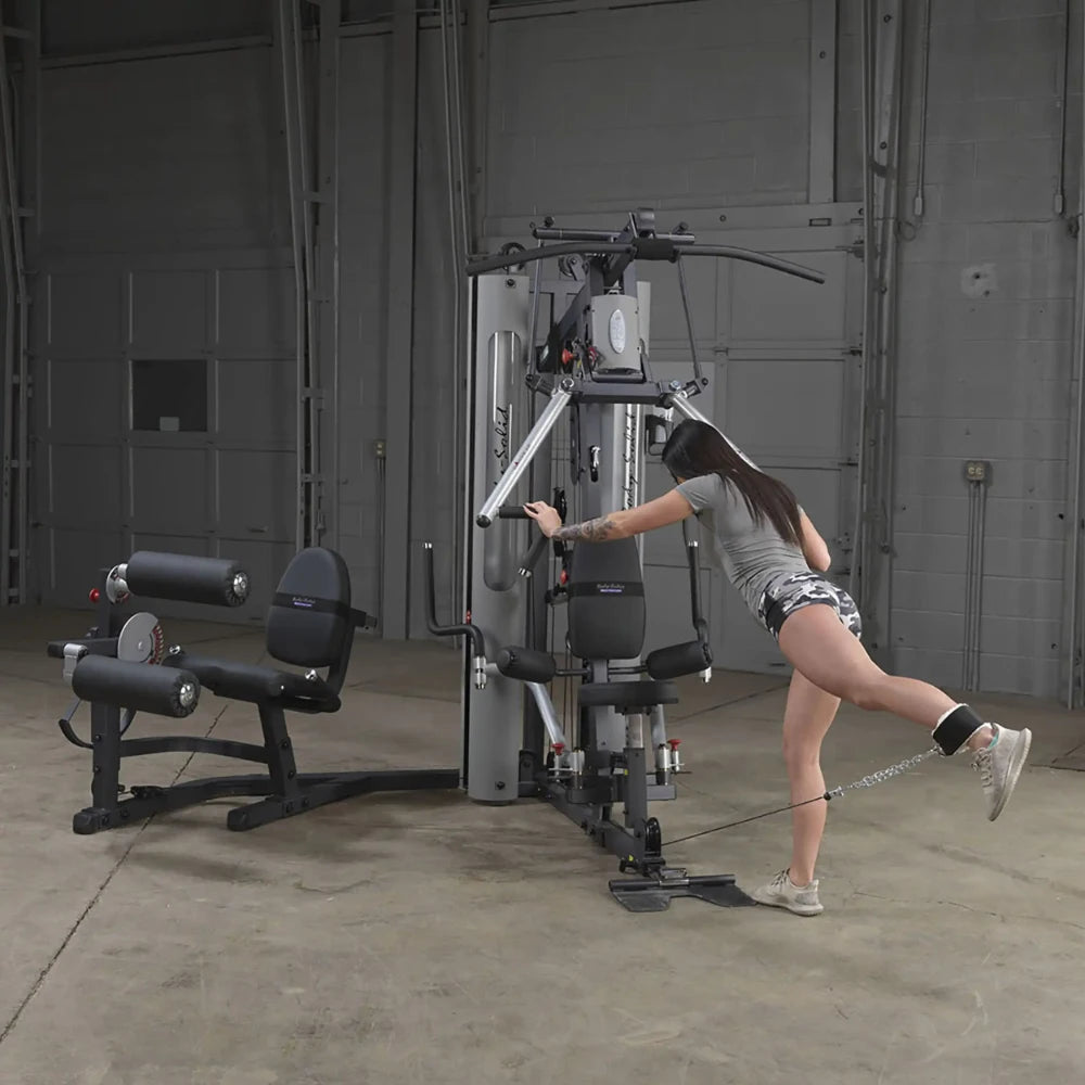 Woman using Body-Solid gym equipment for leg workout in industrial space.
