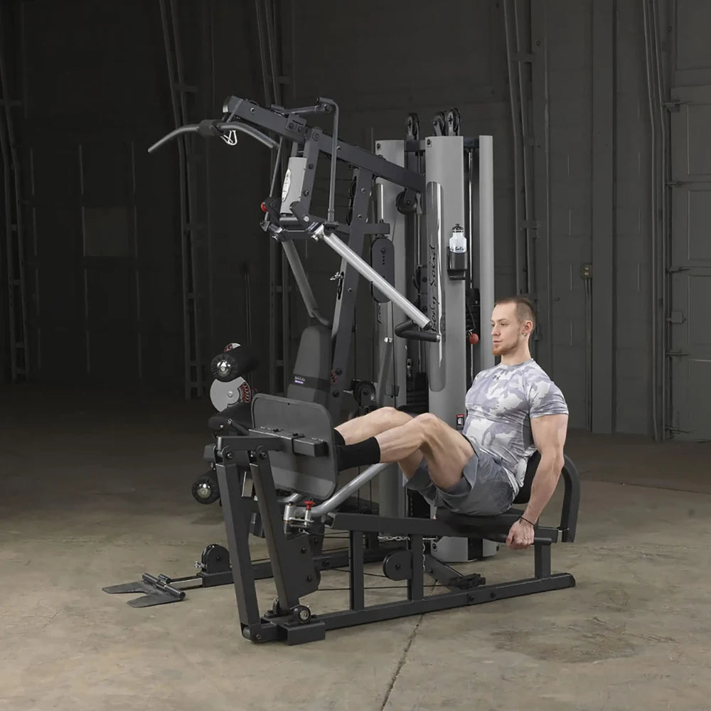 Man using a black multi-gym machine for leg press exercise in a gym setting.