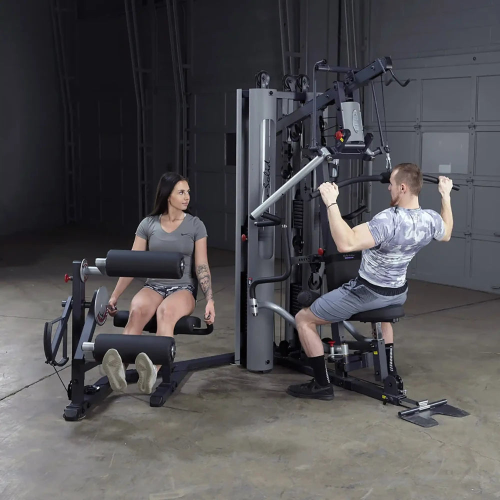 Two people exercising on a Body-Solid gym machine, featuring a multi-station setup for strength training.