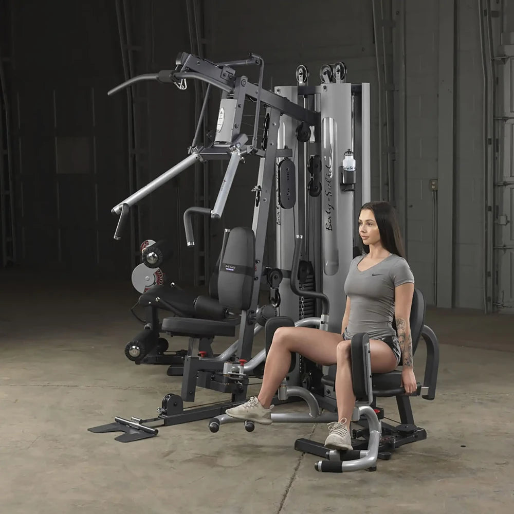 Woman using Body-Solid home gym machine for leg exercises in a gray sports outfit.