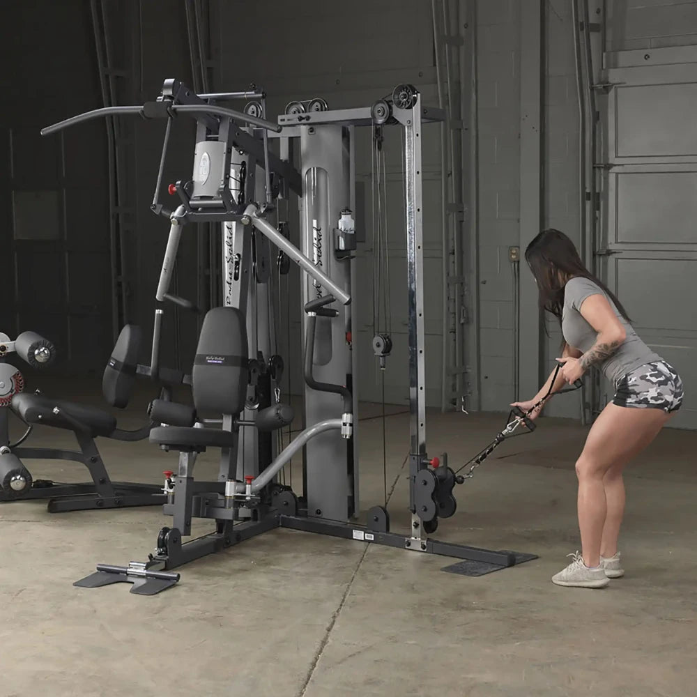 Woman using a Body-Solid home gym machine for cable exercises in a garage setting.