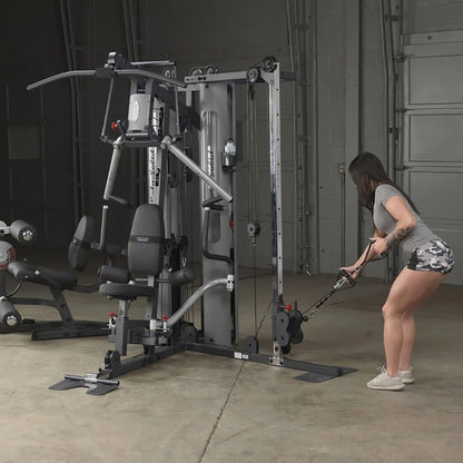 Woman using a Body-Solid home gym machine for cable exercises in a garage setting.