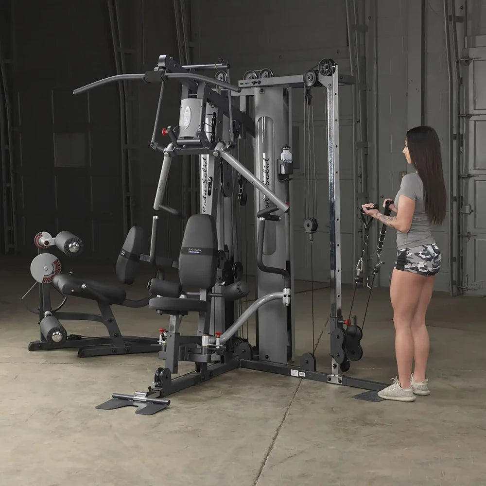 Woman using Body-Solid home gym with pulleys in a garage setting.