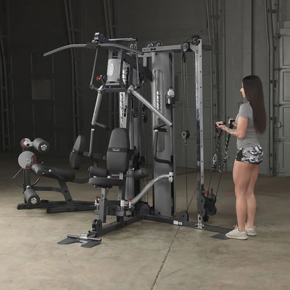 Woman using Body-Solid home gym with pulleys in a garage setting.