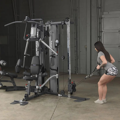 Woman using Body-Solid home gym for cable exercise in gray workout gear.