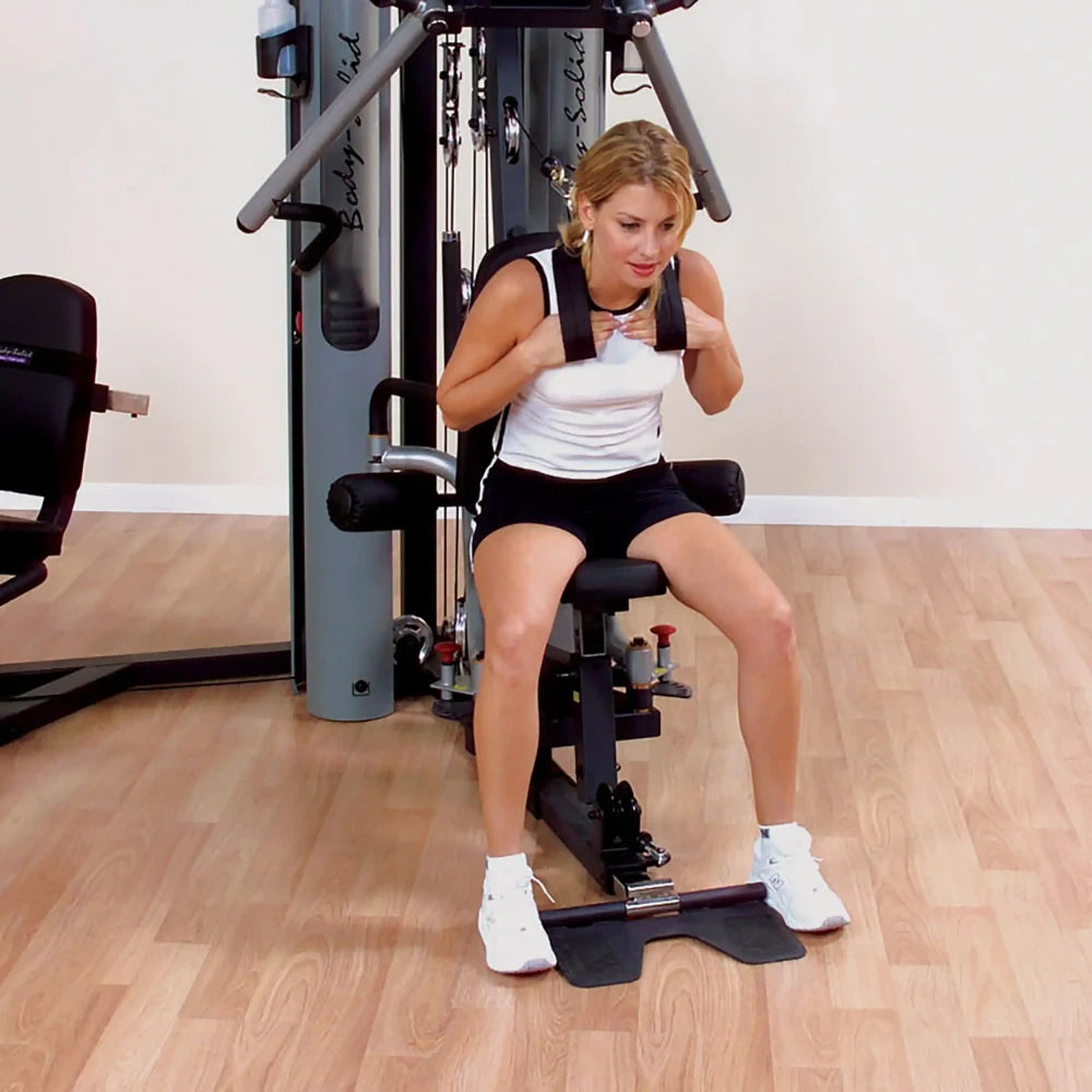 Woman exercising on Body-Solid home gym, wearing white tank top and black shorts.