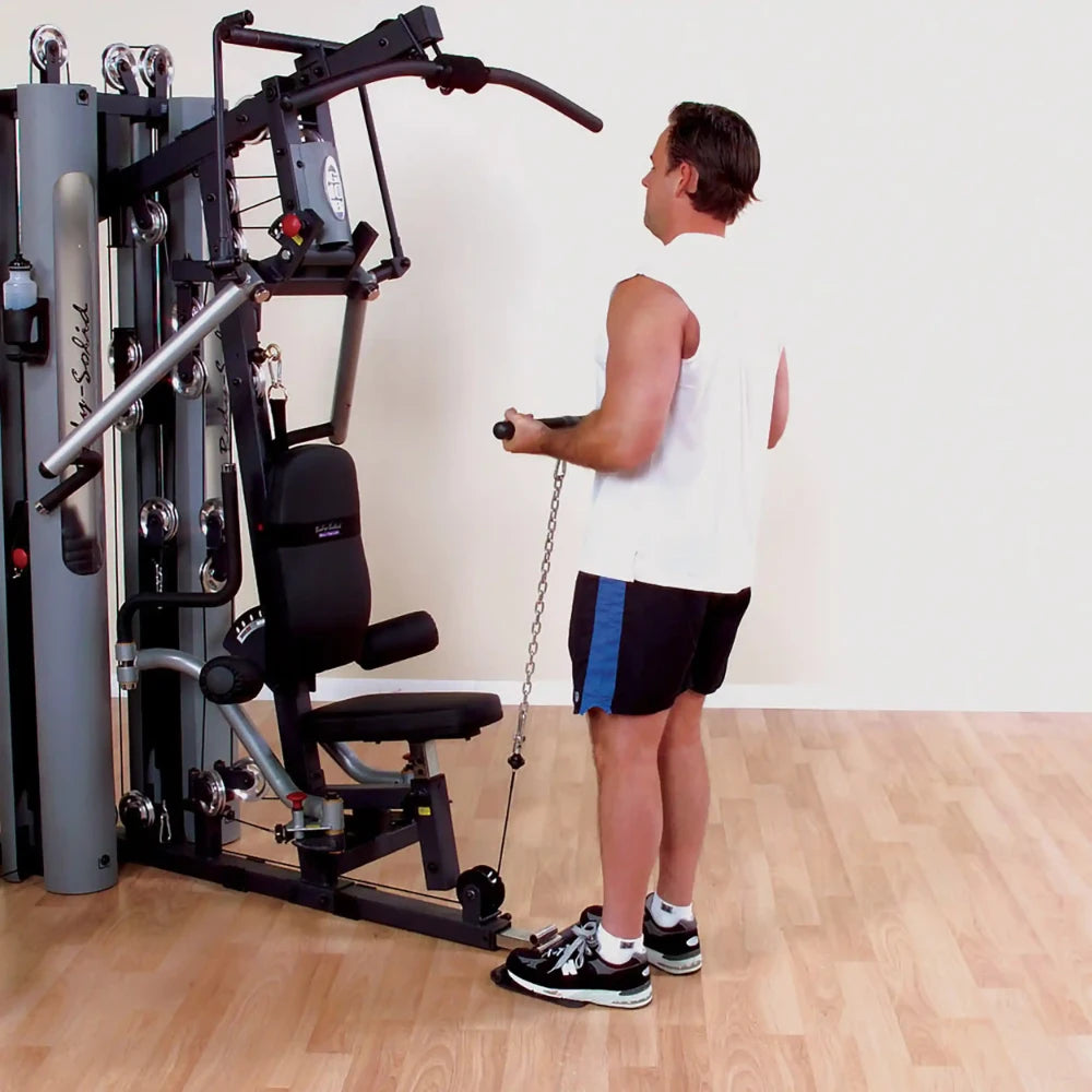 Man using Body-Solid home gym machine in a white tank top and black shorts.