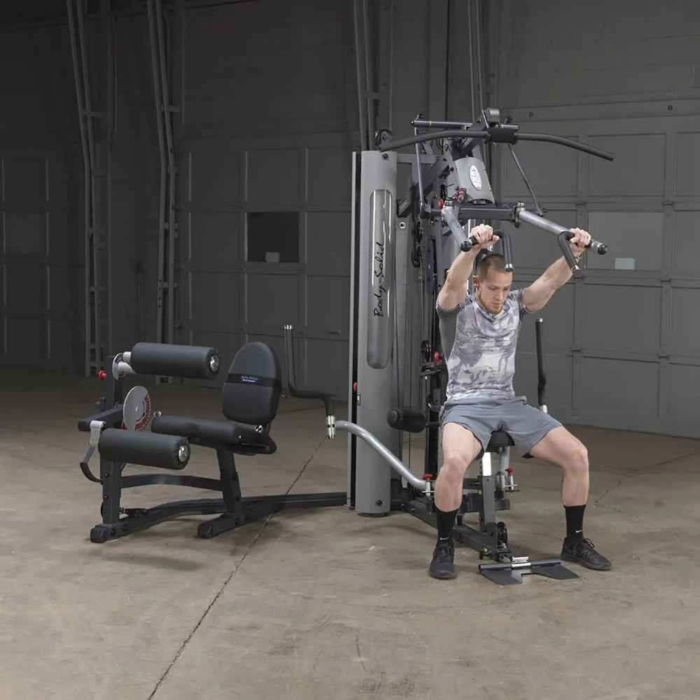 Man using Body-Solid gym machine with adjustable pulleys in a garage gym.