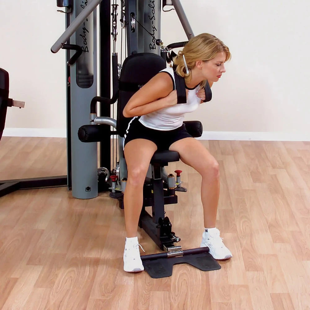 Woman exercising on Body-Solid home gym machine with padded seat in a fitness room.