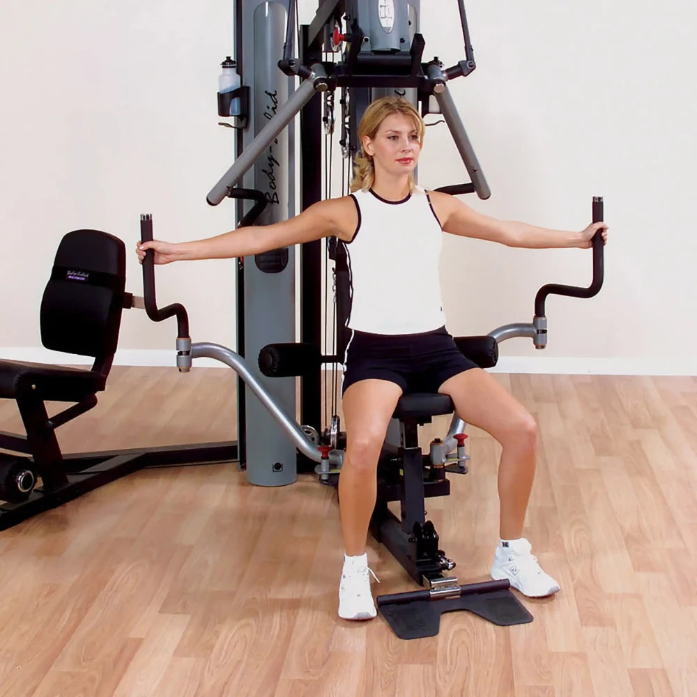 Woman using Body-Solid home gym for arm workout on hardwood floor.