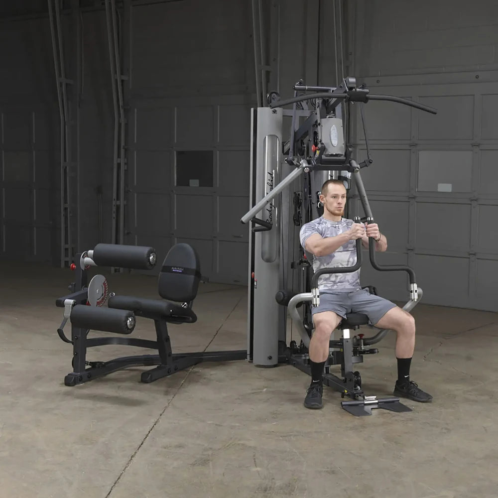 Man using Body-Solid home gym machine with leg press attachment in a garage setting.