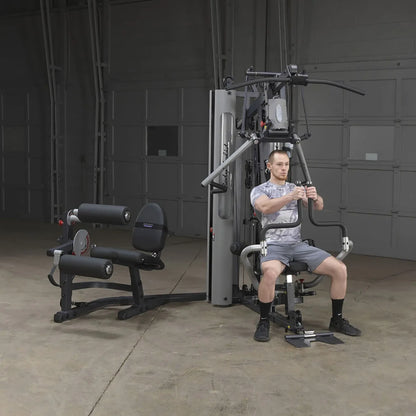 Man using Body-Solid home gym machine with leg press attachment in a garage setting.