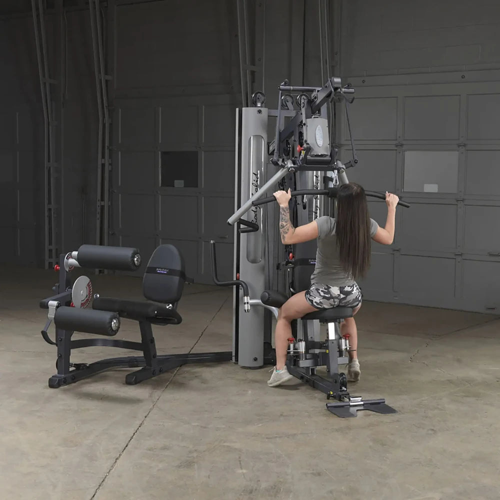 Woman using Body-Solid home gym for lat pulldowns in a garage setting.