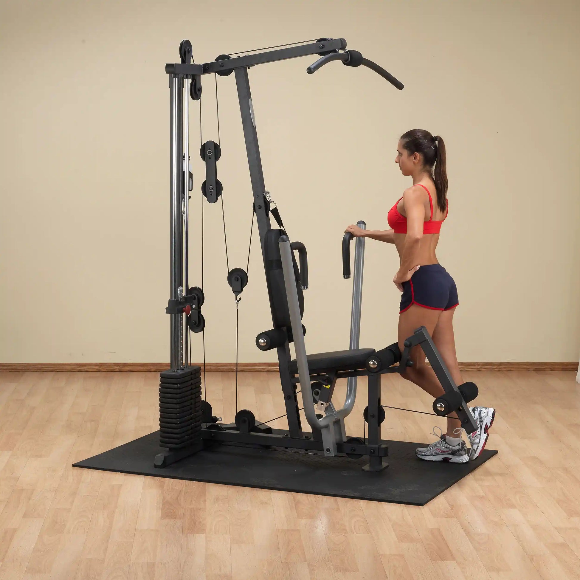 Woman using a home gym machine with weight stack for leg exercises.