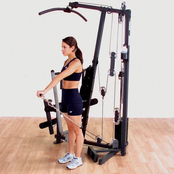 Woman using a multi-gym machine for strength training on wooden floor.