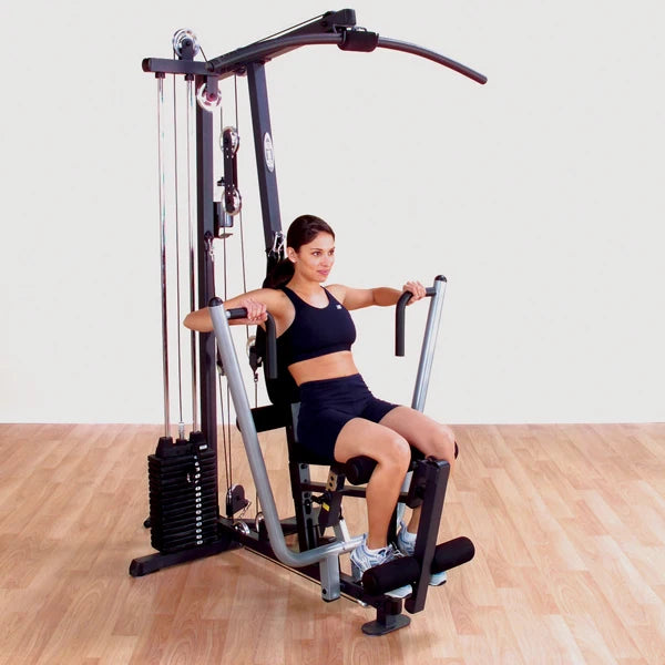 Woman using Body-Solid home gym in black workout gear on wooden floor.