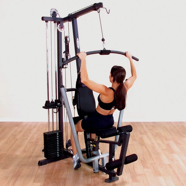 Woman using a home gym for a lat pulldown exercise on wooden flooring.