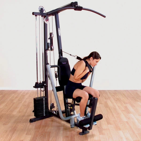 Woman using Body-Solid home gym for strength training on a wood floor.