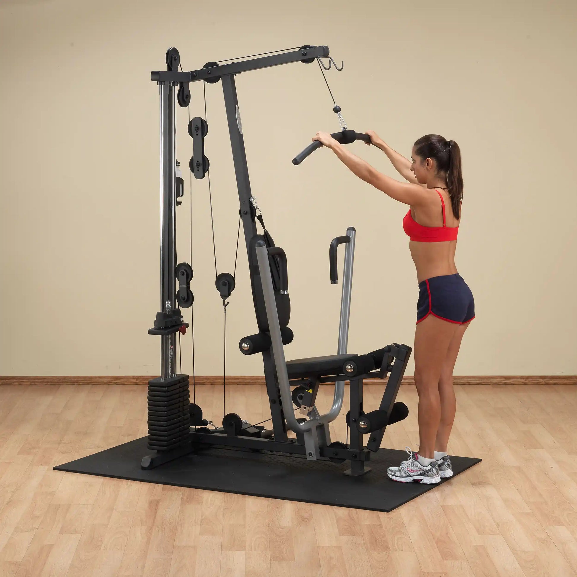 Woman using a home gym machine in a red workout outfit for strength training.