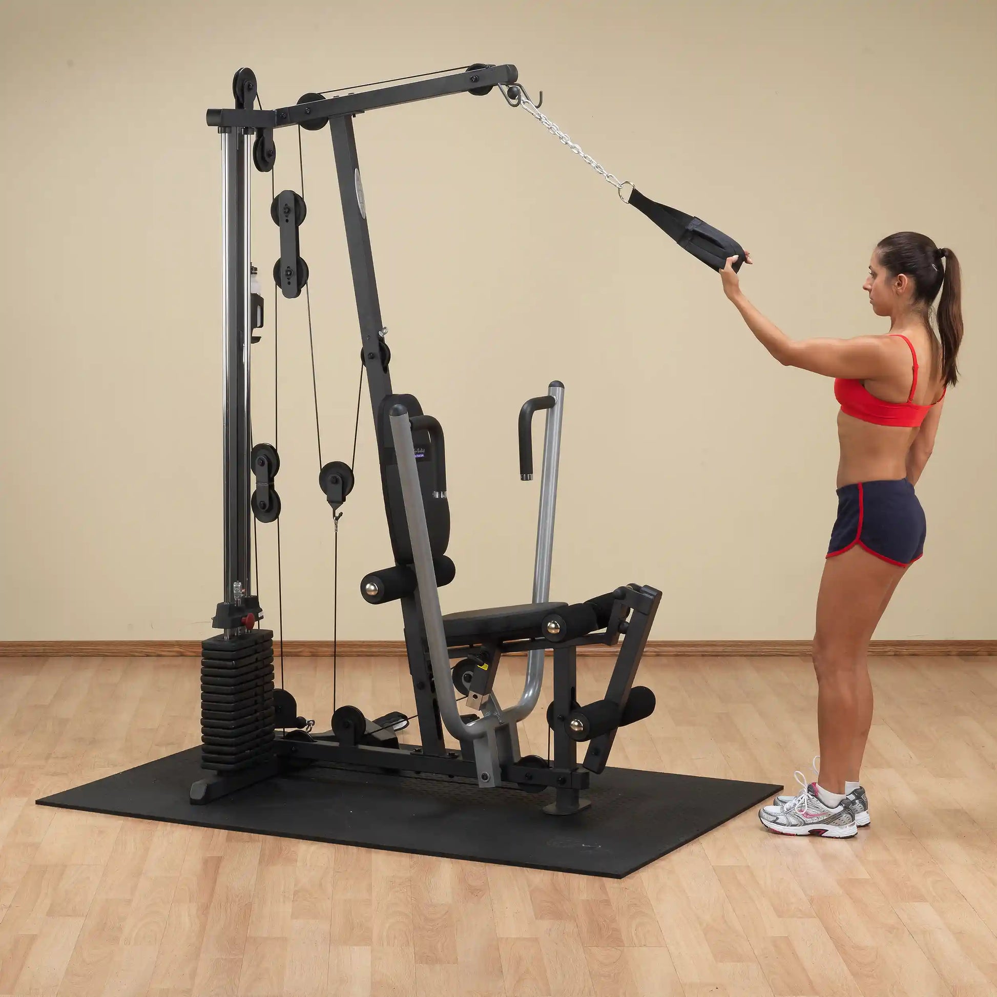 Woman using a black home gym machine for strength training in a workout room.