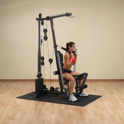 Woman using a home gym machine for leg exercises, wearing a red sports outfit.