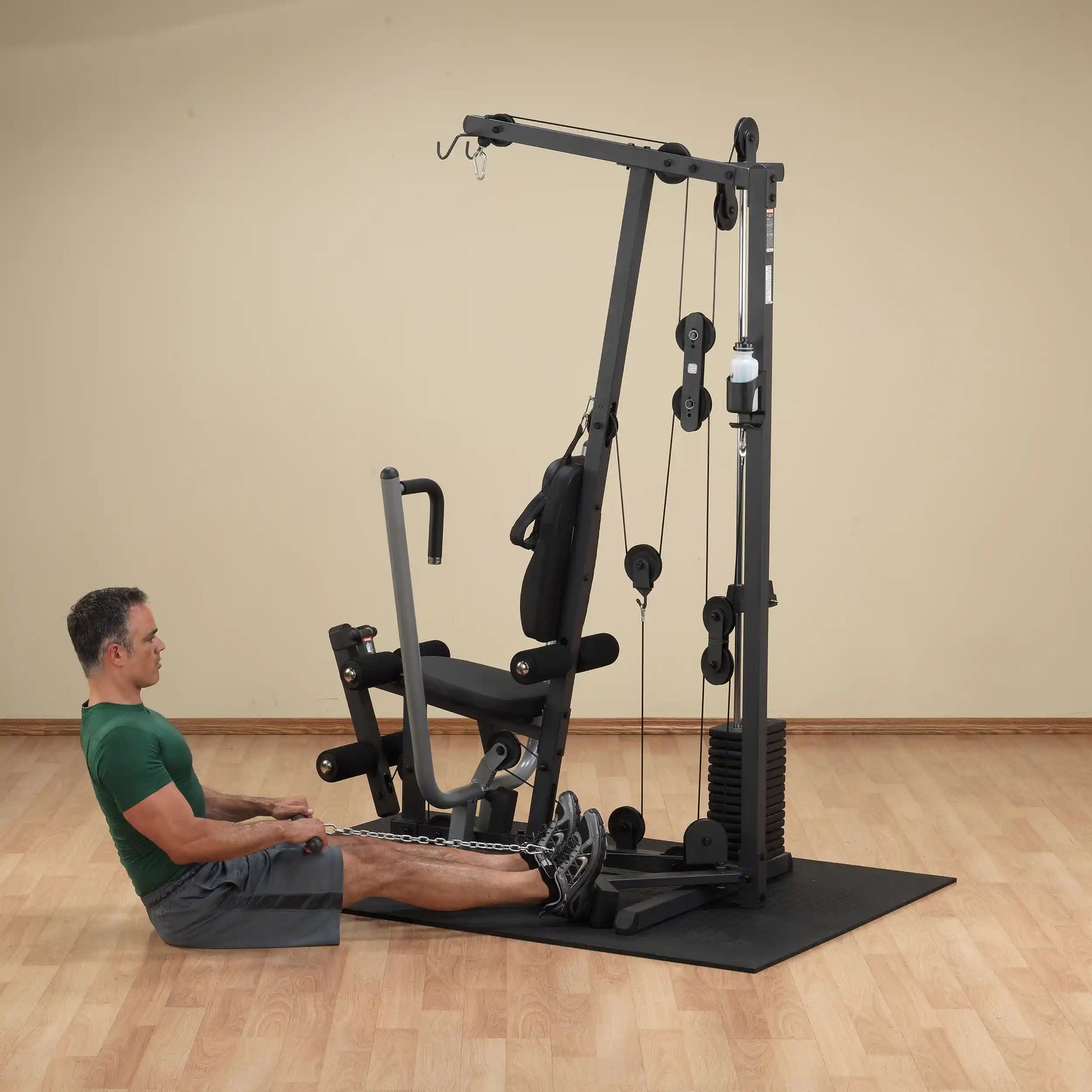 Man using a home gym machine for seated rows on a wooden floor.