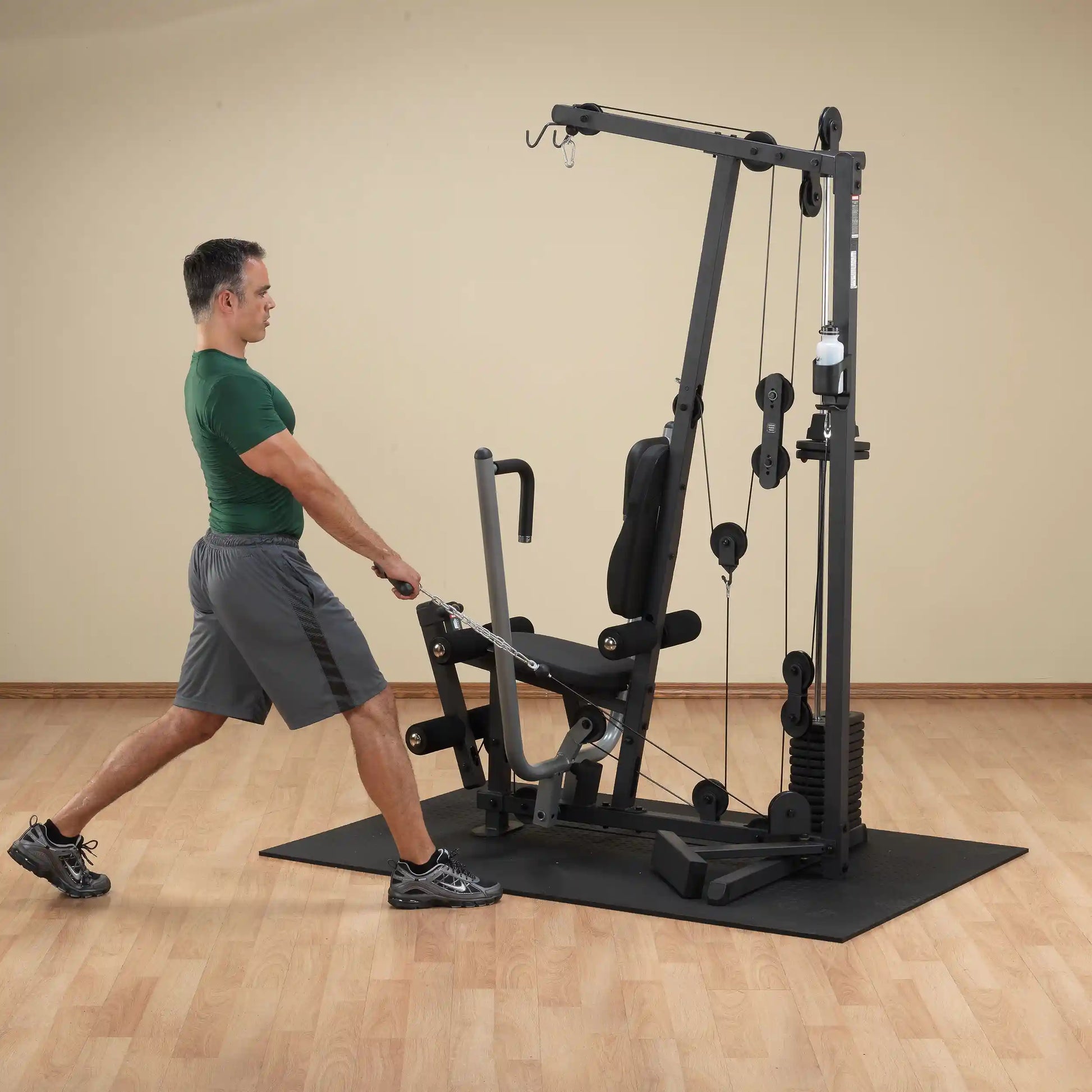 Man using a home gym machine for strength training in a room with wooden floors.
