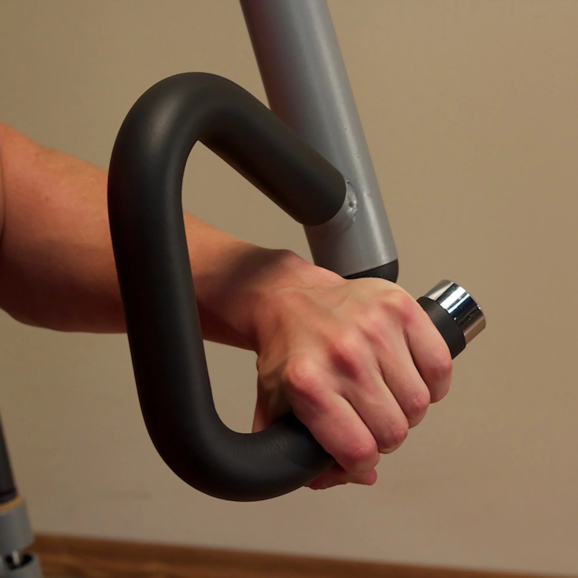 Hand gripping black ergonomic exercise machine handle.