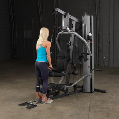 Woman using Body-Solid home gym in bright blue tank, performing cable exercise.