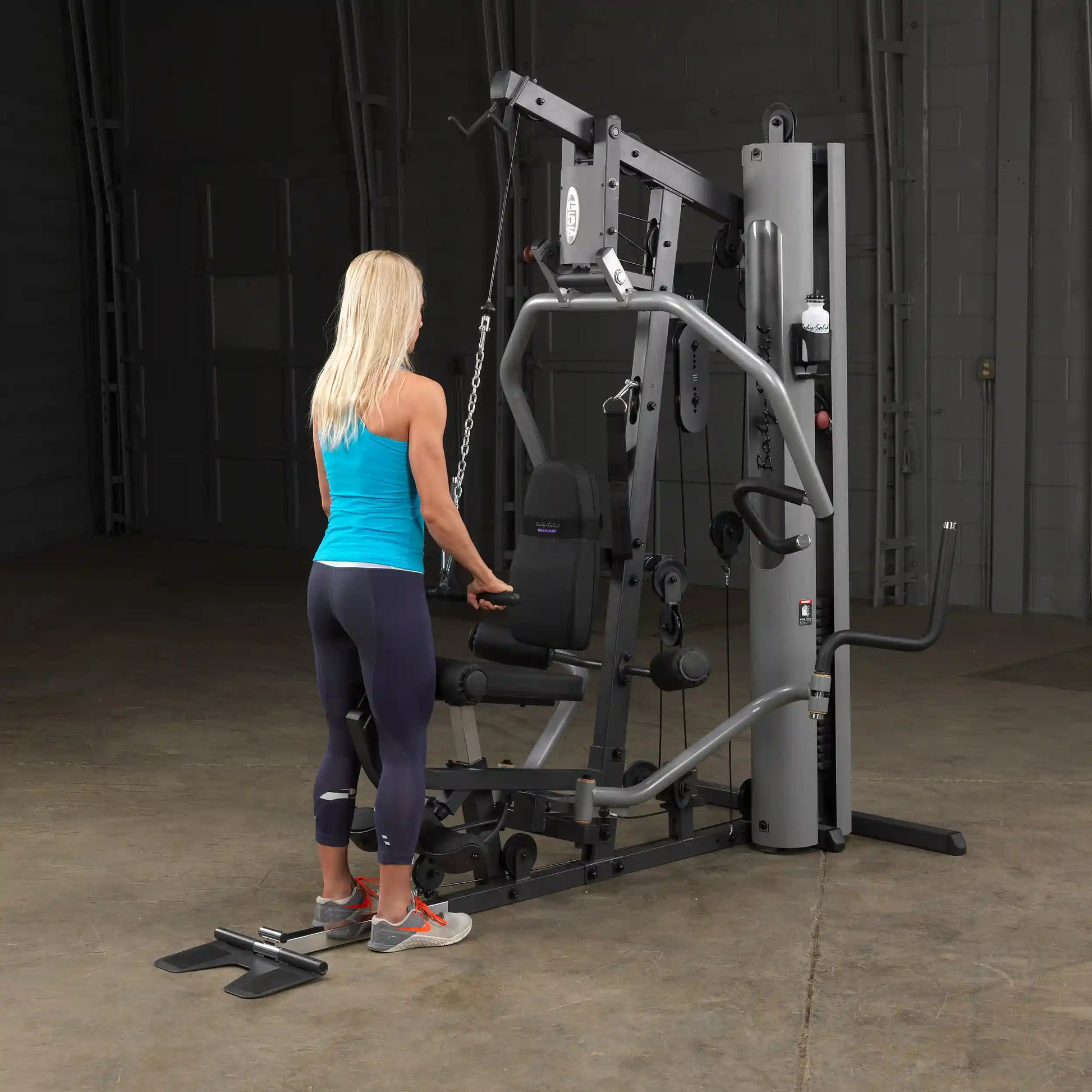Woman using a Body-Solid home gym machine in a blue tank top for strength training.
