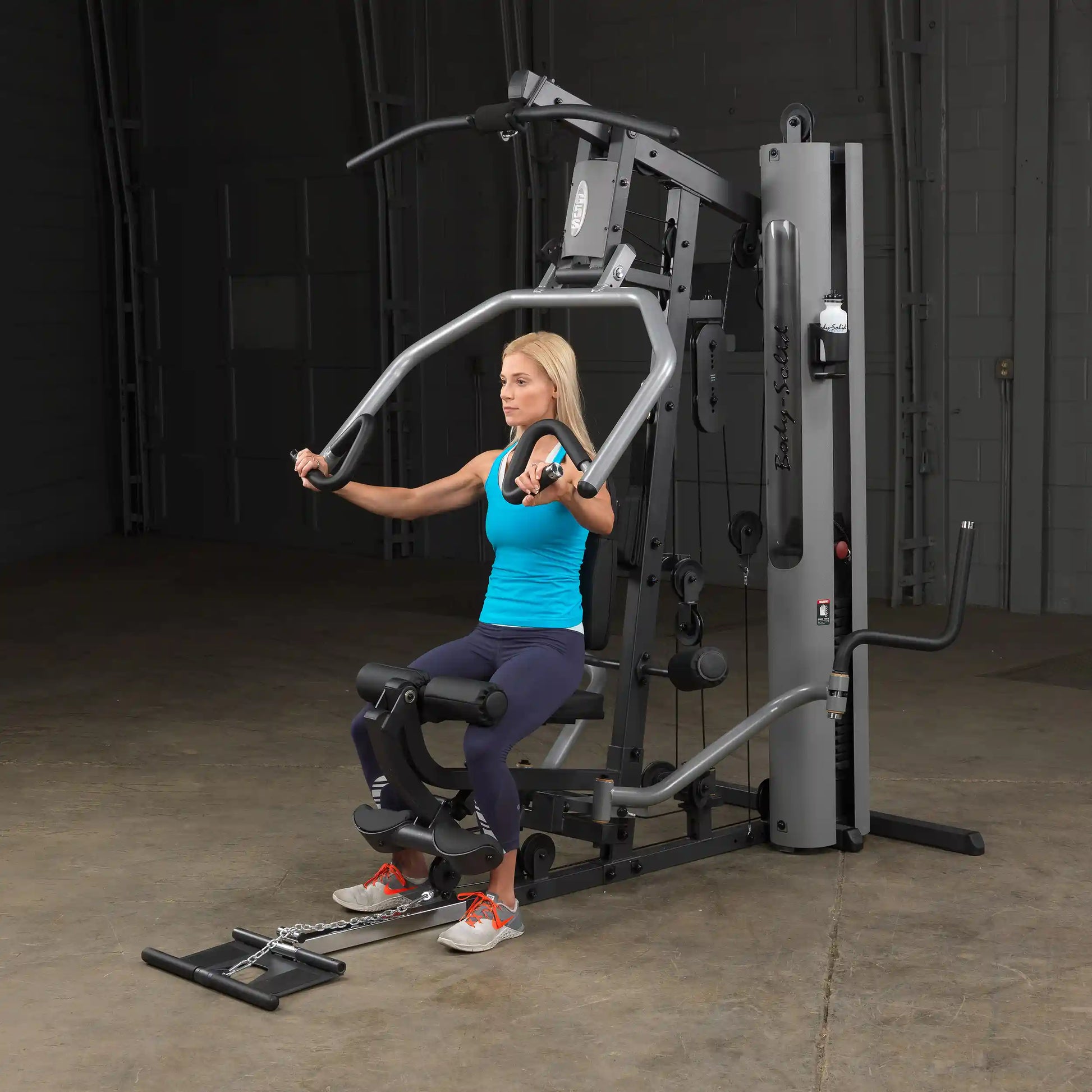 Woman using Body-Solid home gym in blue tank top, performing chest exercises.