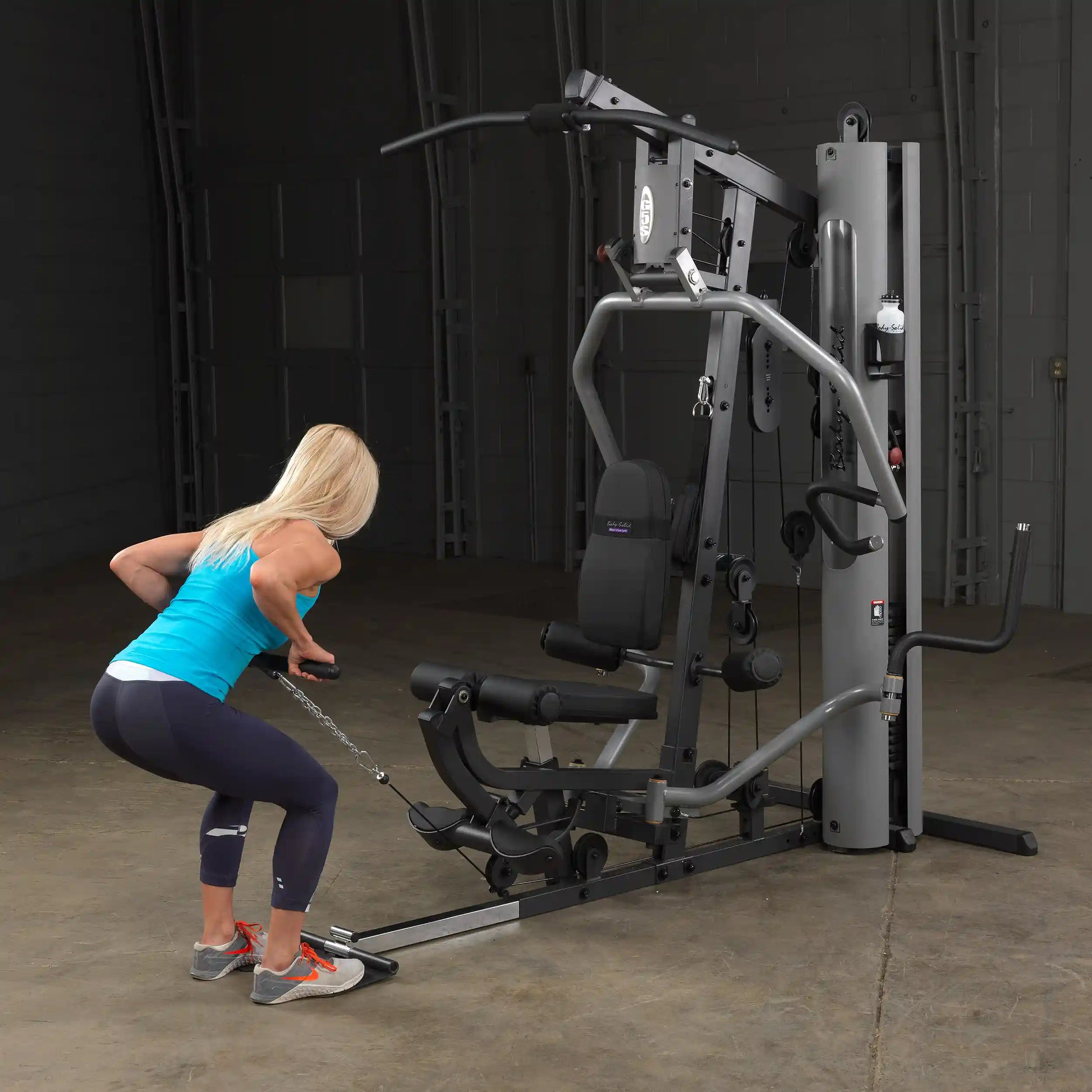Woman using Bowflex home gym for cable exercises in a dimly lit room.