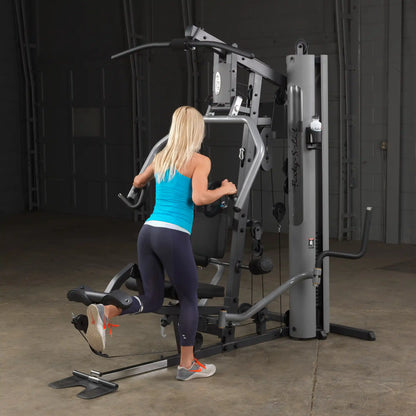 Woman using Body-Solid home gym in blue tank top for leg workout.