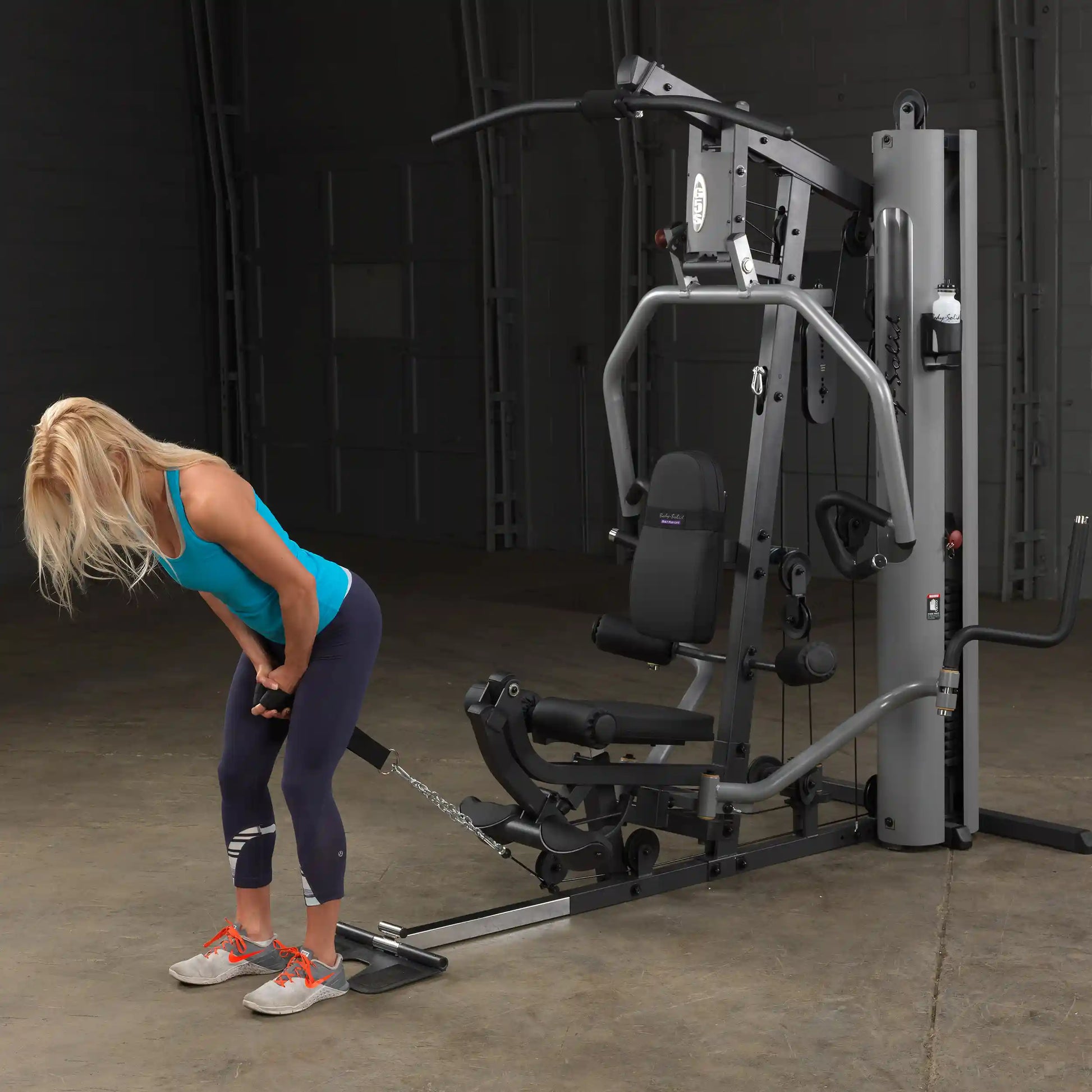 Woman using a Bowflex home gym in a blue tank top and leggings for strength training.